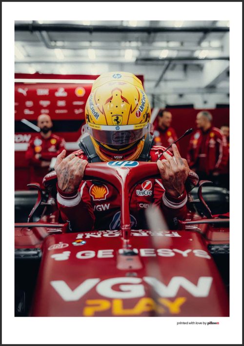 Plagát s Lewisom Hamiltonom v monoposte Ferrari F1 2025, zachytený v garáži pred pretekmi. Ideálny doplnok pre fanúšikov motoršportu.