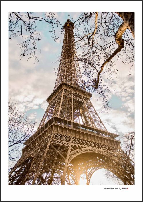Elegantný pohľad na Eiffelovu vežu pri západe slnka so siluetami stromov, ktorý zachytáva atmosféru a krásu Paríža v romantickom svetle.